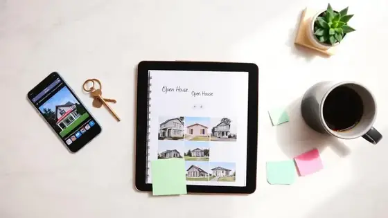 Realtor's desk with a phone showing a property listing, brass house keys, a tablet with home thumbnails, and pastel notes